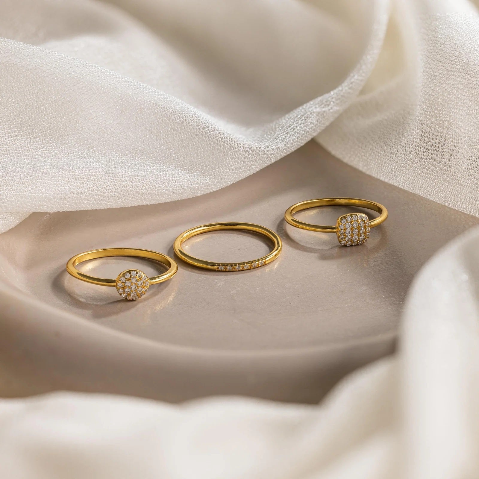 Three gold rings with diamond accents on a soft fabric background
